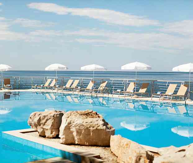 Ulkouima-allas, jonka taustalla aurinkotuoleja ja aurinkovarjoja, meri näkyy altaan alueen takana. (Tekoälyn luoma teksti)