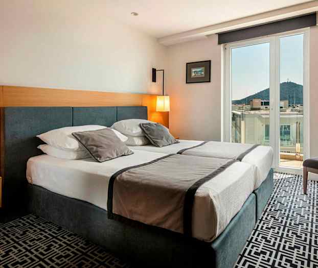 Hotellihuone, jossa on parivuode, vaalea sisustus ja parveke näkymällä kaupunkiin ja vuorille. (Tekoälyn luoma teksti)