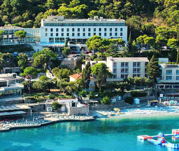 Näkymä hotellirakennuksesta rannikolla, jossa on aurinkotuoleja rannalla ja kelluva leikkipaikka vedessä. (Tekoälyn luoma teksti)