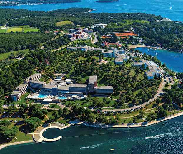 Ilmakuva lomakeskuksesta rannikolla, jossa on vehreää ympäristöä ja näkymä merelle. (Tekoälyn luoma teksti)