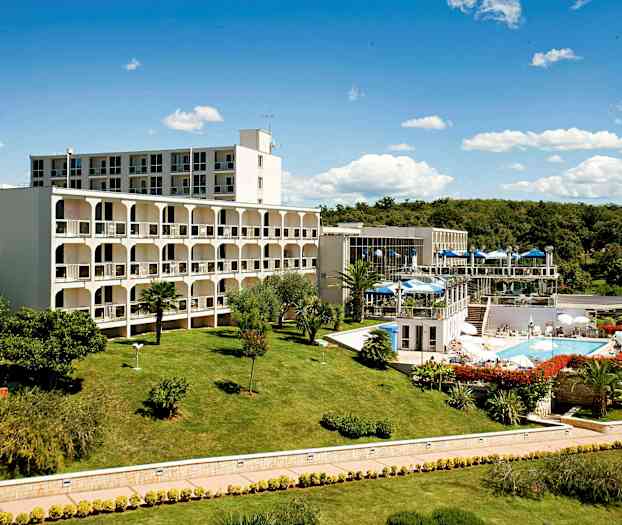 Rakennuskompleksi, jota ympäröi hyvin hoidettu nurmikko ja puutarha, jossa on uima-allas ja ulkoravintola-alueita. (Tekoälyn luoma teksti)