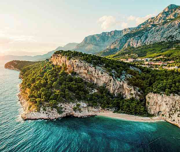 Rannikko jyrkillä kallioilla, metsä ja kirkkaansininen meri. (Tekoälyn luoma teksti)