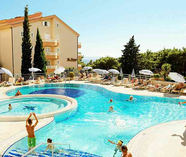 Lomakohde, jossa on uima-allas, ympärillä aurinkotuoleja, aurinkovarjoja ja vihreitä puita. (Tekoälyn luoma teksti)