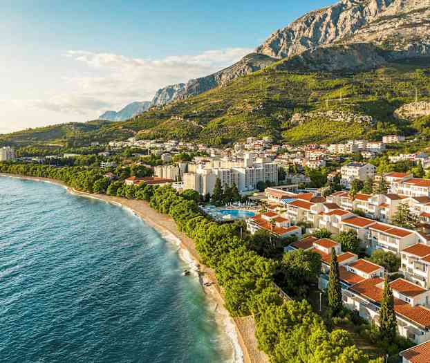 Ilmakuva vuoristomaiseman edessä sijaitsevasta rannikkokaupungista. (Tekoälyn luoma teksti)