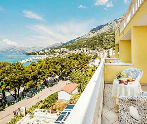 Näkymä keltaisen rakennuksen parvekkeelta kaupungin yli meren äärellä ja ympäröiviin vuoriin. (Tekoälyn luoma teksti)