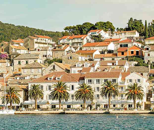 Kuvassa on viehättävä merenrantakaupunki, jossa on punaiset tiilikatot, kivitaloja ja palmuja laiturin varrella. (Tekoälyn luoma teksti)