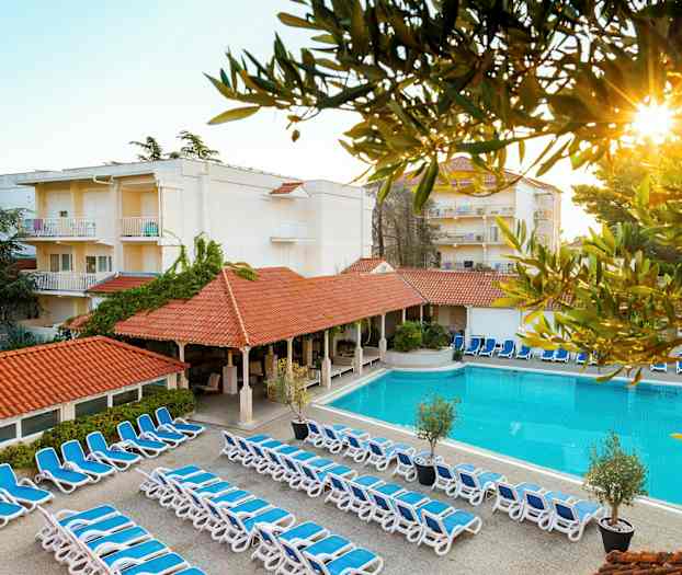 Kuva hotellialueelta, jossa aurinkotuoleja, uima-allas ja rakennuksia. (Tekoälyn luoma teksti)