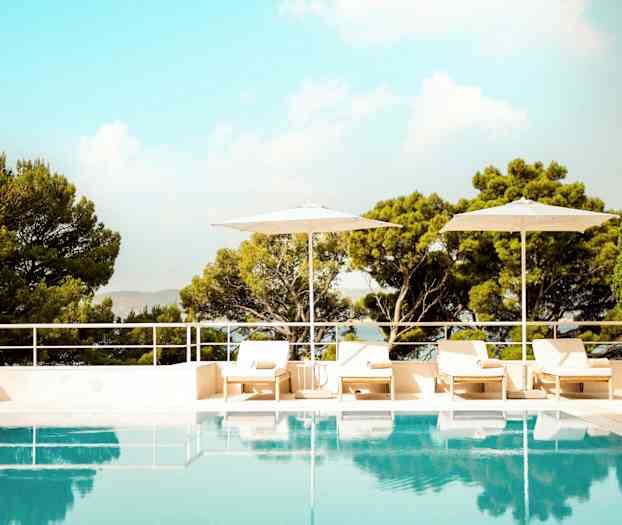 Ulkouima-allas, jota ympäröivät aurinkotuolit, aurinkovarjot ja vehreät puut. (Tekoälyn luoma teksti)