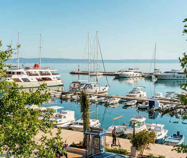 Pienvenesatama, jossa on purjeveneitä ja moottoriveneitä. Joitakin ihmisiä seisoo laitureilla. (Tekoälyn luoma teksti)