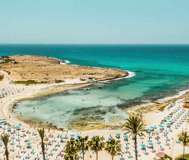 Hiekkaranta, jossa aurinkovarjoja ja uimareita meren äärellä. (Tekoälyn luoma teksti)