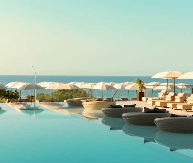 Infinity-allas, jossa on lepotuoleja ja aurinkovarjoja meren äärellä. (Tekoälyn luoma teksti)