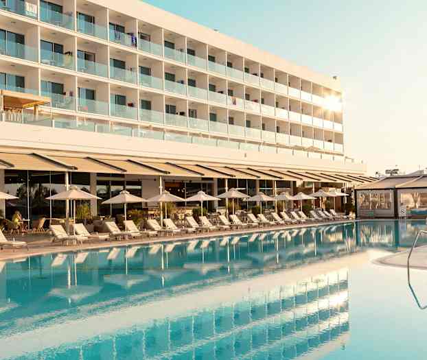 Hotellirakennus parvekkeiden kera näkyy uima-altaan ja aurinkotuolien takana. (Tekoälyn luoma teksti)