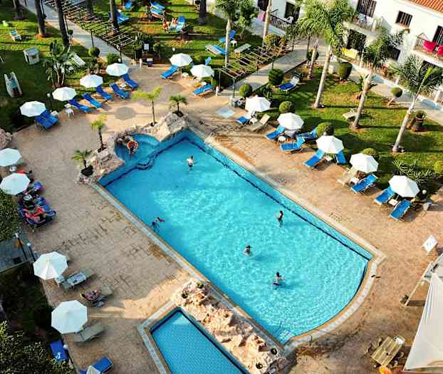 Ilmakuva uima-altaasta, jota ympäröivät aurinkotuolit ja varjot. (Tekoälyn luoma teksti)