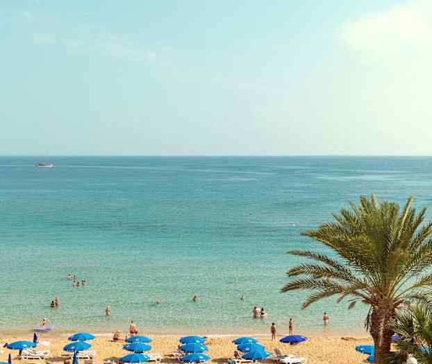 Ranta, jossa on aurinkovarjoja ja ihmisiä veden äärellä. (Tekoälyn luoma teksti)