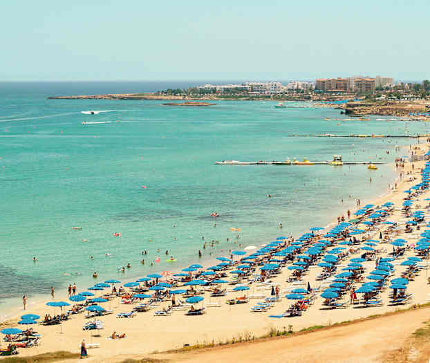 Näkymä rannasta, jossa on sinisiä aurinkovarjoja ja uimareita kirkkaan sinisen meren äärellä. (Tekoälyn luoma teksti)