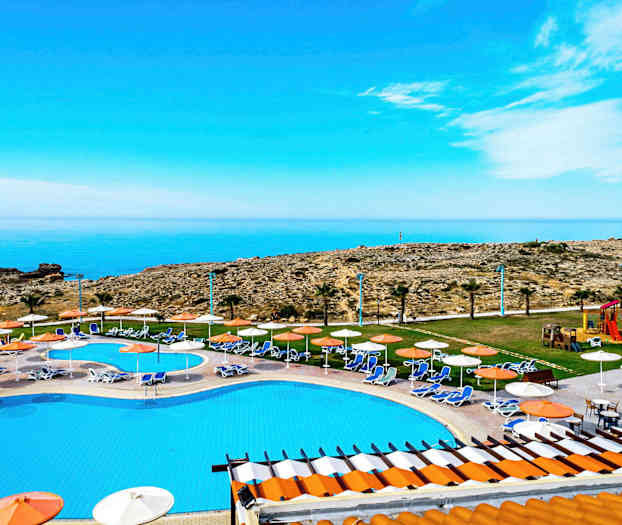 Näkymä uima-altaalle aurinkotuoleilla ja varjolehdillä, kohti merta ja kallioista maisemaa. (Tekoälyn luoma teksti)