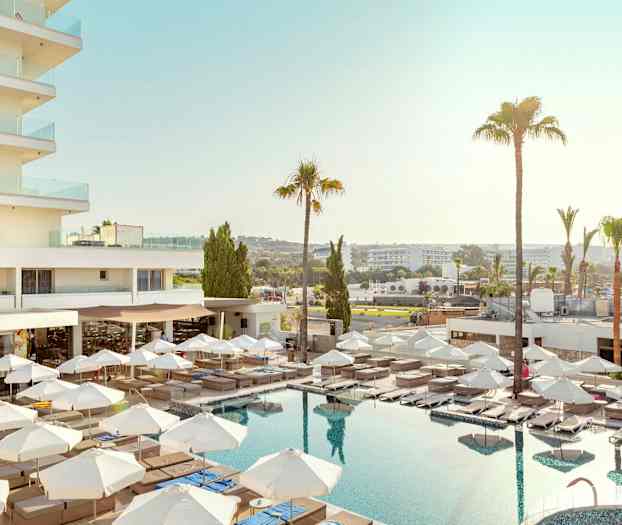 Hotellinäkymä, jossa on uima-allas, aurinkotuoleja ja aurinkovarjoja. (Tekoälyn luoma teksti)