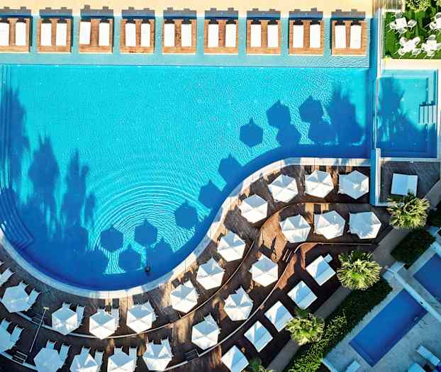 Lintuperspektiivi uima-altaasta, jonka ympärillä on aurinkotuoleja ja -varjoja. (Tekoälyn luoma teksti)