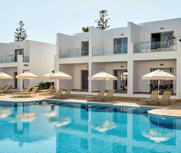 Valkoiset rakennukset terasseineen uima-allasalueella, jossa on aurinkotuoleja ja varjoja. (Tekoälyn luoma teksti)