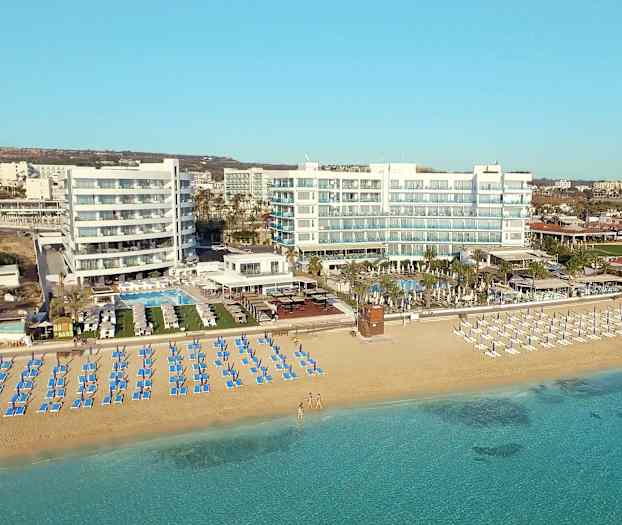 Kuva rannasta, jossa on aurinkotuoleja ja aurinkovarjoja hotellin edustalla rannalla. (Tekoälyn luoma teksti)