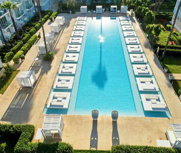 Suorakulmainen uima-allas, jonka ympärillä on aurinkotuoleja ja vihreää aluetta. (Tekoälyn luoma teksti)