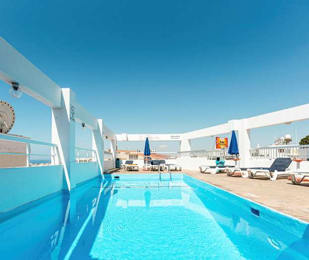 Ulkouima-allas, jossa on aurinkotuoleja ja aurinkovarjoja kirkkaan sinisen taivaan alla. (Tekoälyn luoma teksti)