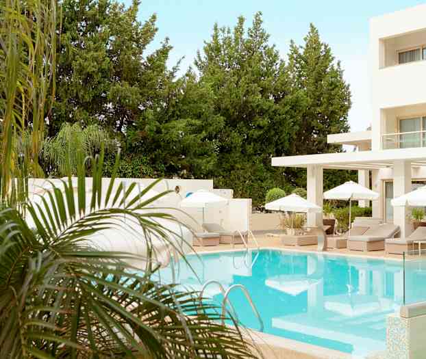 Ulkouima-allas, jonka ympärillä on aurinkotuoleja ja aurinkovarjoja, taustalla vehreitä puita hotellin vieressä. (Tekoälyn luoma teksti)