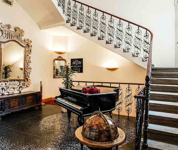 Portaat, joissa on spiraalimainen kaide, piano, maapallo ja suuri koristeellinen peili. (Tekoälyn luoma teksti)