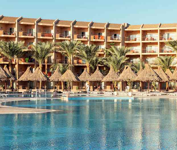 Hotellirakennus parvekkeilla, edessä uima-allas ja palmuja. (Tekoälyn luoma teksti)