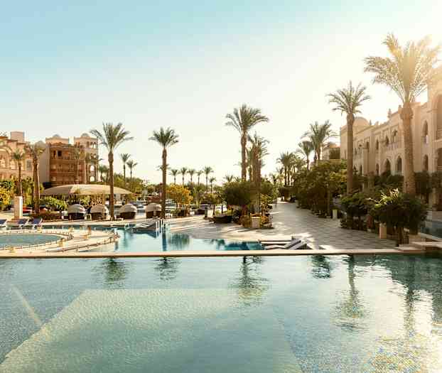 Hotellialue, jossa ulkouima-altaita ja palmurivistöjä rakennusten vieressä. (Tekoälyn luoma teksti)