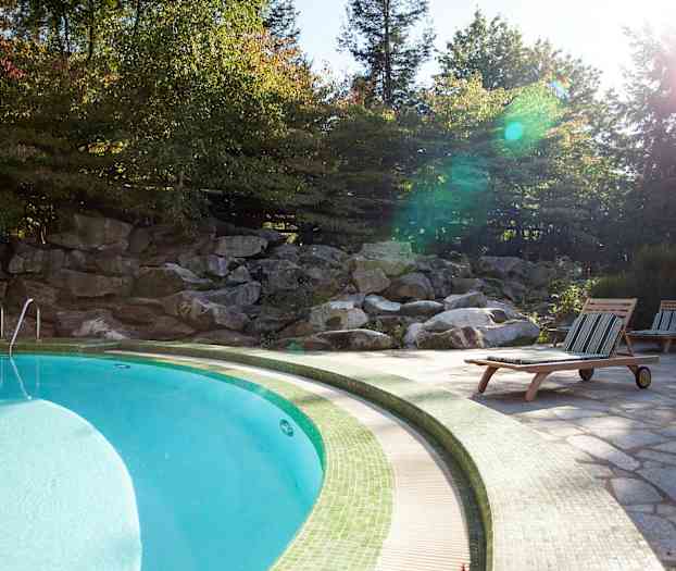 Uima-allas, jonka ympärillä on aurinkotuoleja ja vihreää luontoa. (Tekoälyn luoma teksti)