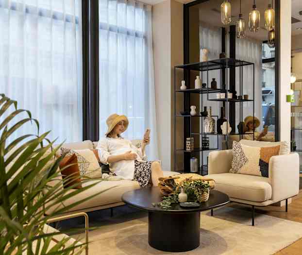 Oleskelutila jossa sohva, pöytä ja hylly koristeilla, sekä kasvi ja lasilamput. (Tekoälyn luoma teksti)