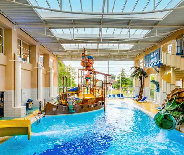 Sisäuima-allas, jossa on merirosvolaiva ja vesiliukumäkiä, ympäröity aurinkotuoleilla ja kasveilla. (Tekoälyn luoma teksti)