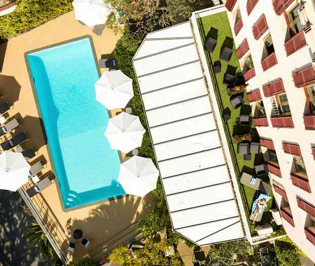 Kuva uima-altaasta, aurinkotuoleista ja aurinkovarjoista rakennuksen vieressä. (Tekoälyn luoma teksti)