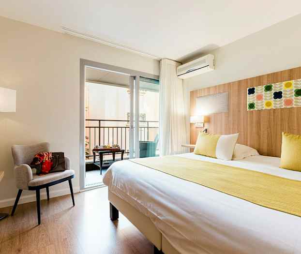 Hotellihuone, jossa on suuri sänky, nojatuoli, kirjoituspöytä ja parveke. (Tekoälyn luoma teksti)