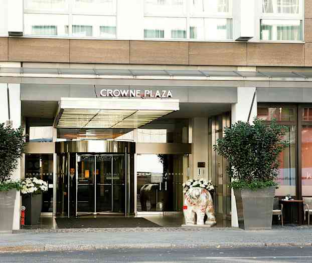 Crowne Plaza -hotellin sisäänkäynti lasiovilla ja suurilla kukkaruukuilla. (Tekoälyn luoma teksti)