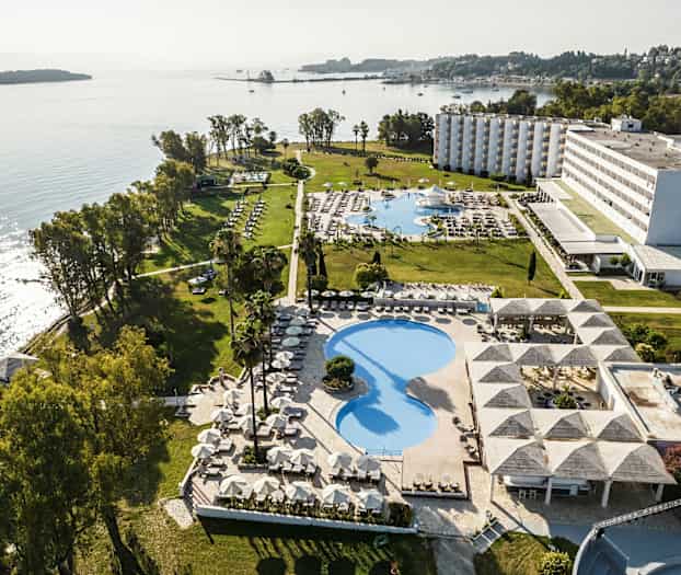 Ilmakuva hotellialueelta meren rannalla, jossa on uima-altaita, viheralueita ja rakennuksia. (Tekoälyn luoma teksti)