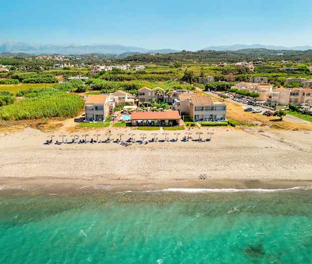 Ilmakuva rannasta, jossa on aurinkovarjoja ja lomakeskus. (Tekoälyn luoma teksti)