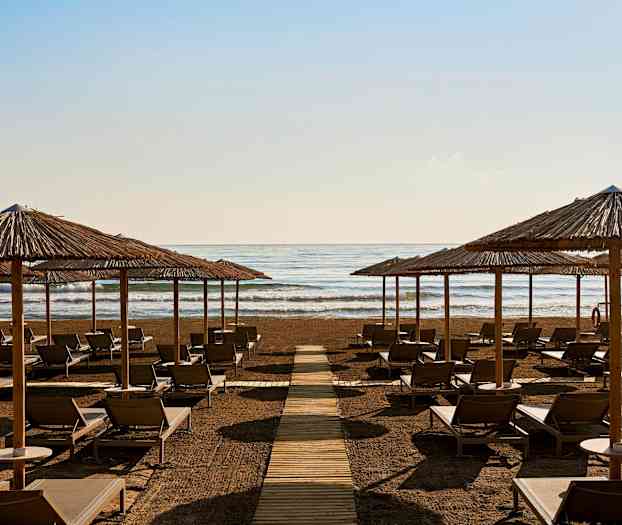 Aurinkotuoleja ja aurinkovarjoja rannalla meren edessä. (Tekoälyn luoma teksti)