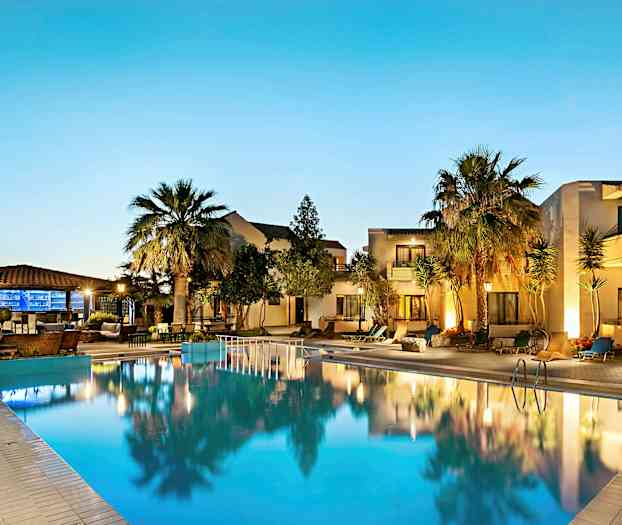 Valaistu uima-allas hotellin edessä, ympärillä palmuja ja terassi hämärässä. (Tekoälyn luoma teksti)