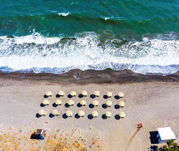 Ilmakuva rannasta, jossa aurinkovarjoja ja aaltoja. (Tekoälyn luoma teksti)