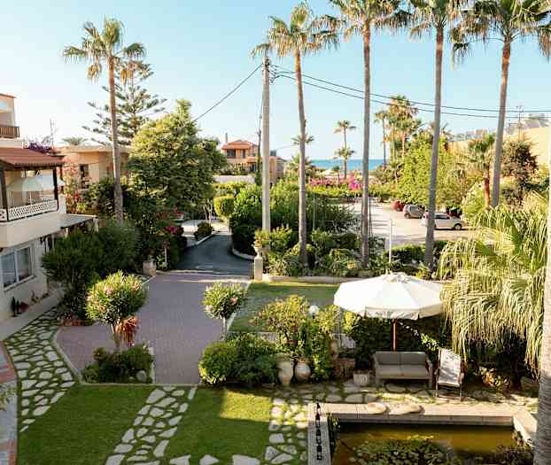 Kuva puutarhasta, jossa on sohva ja varjo lähellä pientä lampea, ympäröidynä palmuilla ja kasvillisuudella. (Tekoälyn luoma teksti)