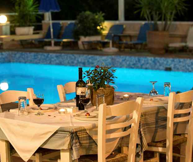 Katettu pöytä valkoisten tuolien kanssa valaistun uima-altaan vierellä. (Tekoälyn luoma teksti)