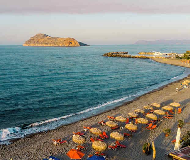 Ranta aurinkovarjoineen ja aurinkotuoleineen meren rannalla. Taustalla kallio. (Tekoälyn luoma teksti)