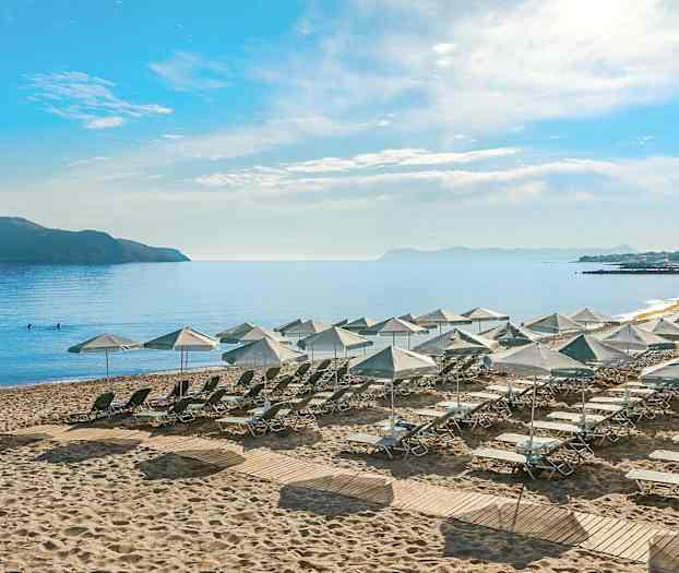 Näkymä rannalle, jossa aurinkotuoleja ja -varjoja, ympäröivä meri ja kaukainen saari. (Tekoälyn luoma teksti)