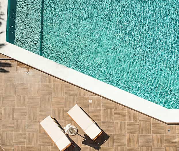 Kaksi aurinkotuolia puulattialla uima-altaan vieressä. (Tekoälyn luoma teksti)