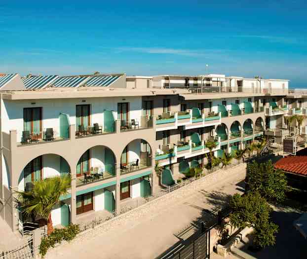 Kuva hotellista, jossa on parvekkeita ja arkkitehtonisia kaaria, ympäröitynä vehreydellä. (Tekoälyn luoma teksti)