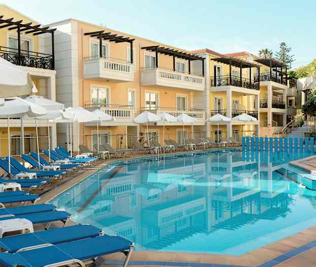 Pastellinsävyinen hotellin julkisivu parvekkeineen, edessä sininen uima-allas, jota ympäröivät aurinkotuolit ja aurinkovarjot. (Tekoälyn luoma teksti)
