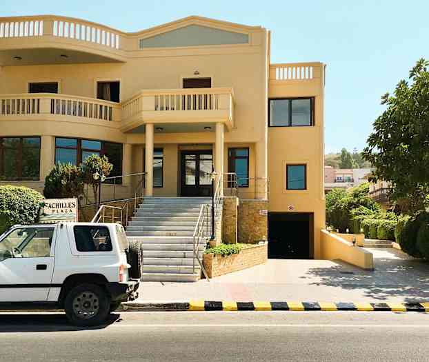 Auto on pysäköity rakennuksen eteen, jossa on kyltti, jossa lukee 'Achilles Plaza'. (Tekoälyn luoma teksti)