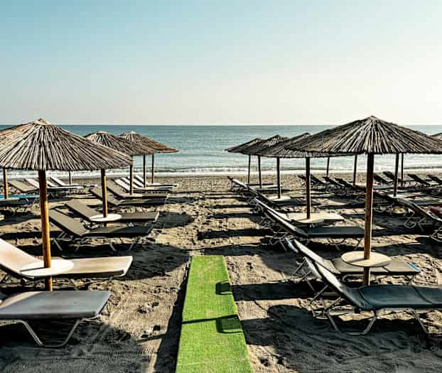 Ranta, jolla aurinkotuoleja ja aurinkovarjoja rivissä meren äärellä. (Tekoälyn luoma teksti)